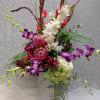 Tall floral arrangement with purple orchids, white orchids, and red tropical blooms in a white vase