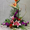 Tall tropical flower arrangement with orange bird of paradise and purple orchids in a glass vase