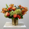 An elegant arrangement in a gold vase featuring vibrant mokara orchids, lush