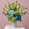 Blue and white hydrangeas in a white vase with tall green and white spikes