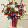 Red roses and white chrysanthemums in a glass vase with a red and blue ribbon
