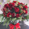 Red rose arrangement in a glass vase with pinecones and a red ribbon
