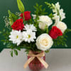 Red and white roses with daisies in a pink vase with a gold ribbon