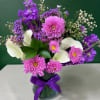 Purple and pink mixed bouquet with white calla lilies in a glass vase
