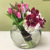 Pink tulips and burgundy orchids in a round glass vase