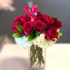 Red roses in a clear square vase with white hydrangeas and a butterfly pick