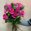Handheld bouquet of bright pink roses with small white filler flowers