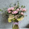 Pink and cream flowers in a glass vase with a lavender ribbon