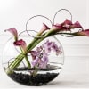 Calla lilies and purple orchids in a round glass bowl with black stones
