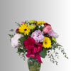 Mixed bouquet of pink, yellow, and lavender flowers in a glass vase with a ribbon