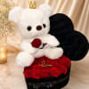 White teddy bear with a crown sitting on red roses in a black heart box