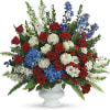 Red roses, blue flowers, and white blooms arranged in a white urn vase