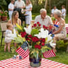 Red roses and white lilies in a glass vase with small American flags