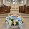White flower basket with blue ribbons and a teddy bear in a church