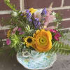Mixed bouquet in a floral teacup and saucer with yellow, purple, pink, and white blooms