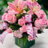 Pink lilies, roses, and carnations in a green vase with ribbon
