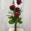 Four red roses in a clear glass vase with greenery
