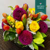 Bouquet of yellow roses, orange tulips, and purple dahlias in a glass vase