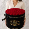 Woman holding a large round box of red roses with a black ribbon
