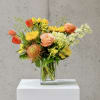Mixed bouquet in a clear glass vase with orange, yellow, and peach flowers