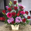 Mixed bouquet of red roses, pink daisies, and lilies in a white vase