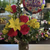 Birthday bouquet of red roses and yellow lilies in a glass vase with a balloon