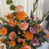 Orange and peach floral arrangement in a pink hatbox with ribbon
