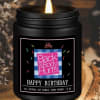 Black jar candle with a lit flame and birthday label