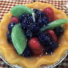 A fruit tart topped with blueberries, strawberries, and green fruit slices