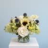 White roses and a sunflower in a glass vase with blue thistle accents