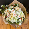 Bouquet of white and peach flowers wrapped in newspaper-style paper