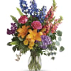 Colorful mixed bouquet in a clear glass vase with lilies, roses, and blue flowers