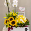 Yellow and white floral arrangement with orchids, sunflowers, and roses in a white box