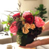 Handheld bouquet of pink and red roses in a black vase