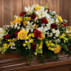 Large floral casket spray with white lilies, yellow roses, and red carnations