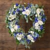 Heart-shaped floral wreath with white and blue flowers on a black stand