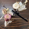 Two small dried floral boutonnieres with ribbon ties on a wooden surface