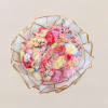 Round bouquet of pink, peach, and white flowers wrapped in white paper with gold trim.