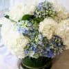 White and blue hydrangea arrangement in a green glass vase