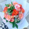 Handheld bouquet of orange and pink roses wrapped in white translucent paper.