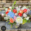 Mixed bouquet of peach roses, blue hydrangea, white peony and calla lilies in a patterned vase.