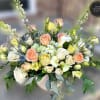 Low ceramic bowl of white, peach, and yellow roses, calla lilies, and mixed blooms in a lush arrangement.