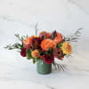 Orange and burgundy floral arrangement in a green vase