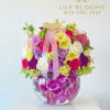 Colorful mixed flower arrangement in a round glass vase with a pink ribbon