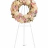 Pastel floral wreath on a white stand with pink and cream roses