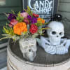 Colorful bouquet in a skull-shaped vase beside a decorative skull