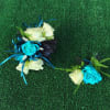 Two small rose corsages with blue ribbon accents on green turf