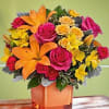 Bright bouquet of orange lilies, pink roses, and yellow flowers in a square vase