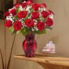 Red roses arranged in a red glass vase with white filler flowers