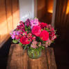 A lush, rounded bouquet of pink, red, and purple blooms that reads